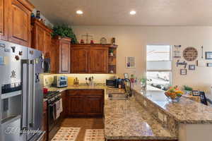 Kitchen with a peninsula, stainless steel appliances, light stone countertops, dark tile patterned flooring, and a textured ceiling