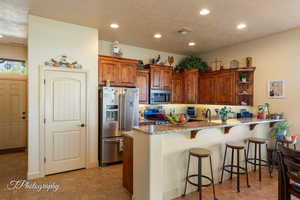 Kitchen featuring a peninsula, light stone counters, stainless steel appliances, brown cabinetry, and a breakfast bar area