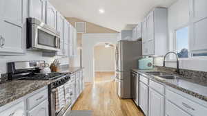 Kitchen featuring stainless steel appliances, light wood finished floors, a ceiling fan, lofted ceiling, and dark stone countertops