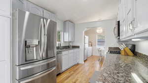 Kitchen featuring stainless steel appliances, dark stone counters, light wood-type flooring, arched walkways, and crown molding