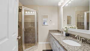 Full bath with light tile patterned flooring, a stall shower, and double vanity