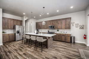 Kitchen with a kitchen breakfast bar, appliances with stainless steel finishes, decorative backsplash, hanging light fixtures, and an island with sink