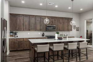 Kitchen featuring appliances with stainless steel finishes, recessed lighting, hanging light fixtures, a center island with sink, and backsplash