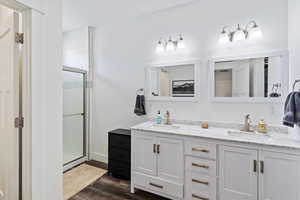 Bathroom featuring a stall shower, double vanity, and dark wood finished floors