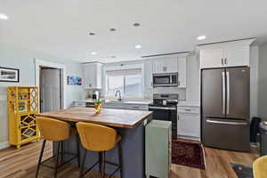 Kitchen featuring stainless steel appliances, white cabinets, a breakfast bar, butcher block counters, and recessed lighting