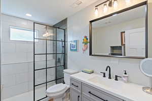 Bathroom with tiled shower, vanity, and recessed lighting