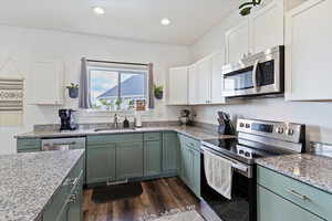 Kitchen featuring green cabinets, appliances with stainless steel finishes, light stone counters, dark wood-type flooring, and recessed lighting