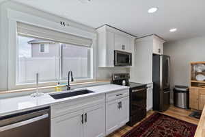 Kitchen with appliances with stainless steel finishes, light wood-style floors, white cabinetry, recessed lighting, and light stone counters