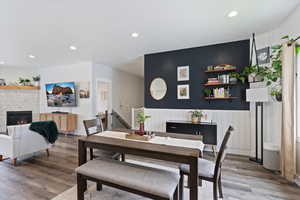 Dining room featuring recessed lighting, wood finished floors, a stone fireplace, and wainscoting