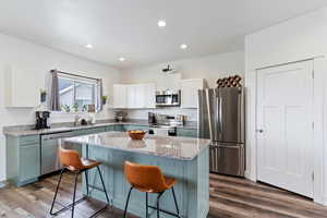 Kitchen with appliances with stainless steel finishes, white cabinets, dark wood-style floors, light stone counters, and a breakfast bar area
