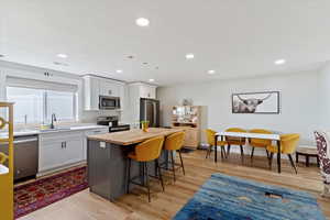 Kitchen featuring butcher block countertops, a kitchen breakfast bar, appliances with stainless steel finishes, a kitchen island, and light wood-style floors