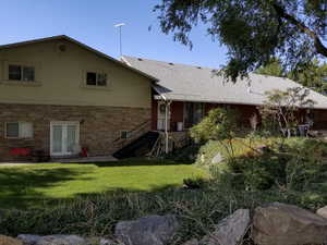 Back of property with a patio area, stone siding, a lawn, french doors, and stucco siding