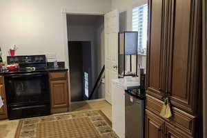 Kitchen featuring electric range, dark countertops, refrigerator, and brown cabinets
