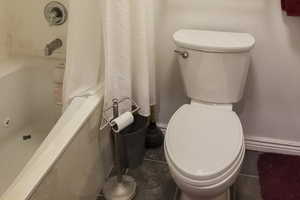Full bathroom featuring toilet and shower / bathtub combination with curtain