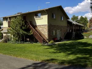 Back of property featuring stone siding, stucco siding, a lawn, and stairs