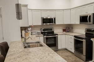 Kitchen featuring stainless steel appliances, decorative backsplash, white cabinetry, and light stone counters