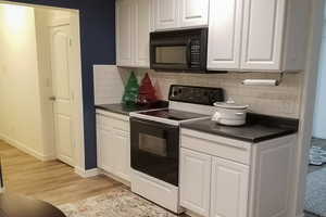 Kitchen featuring dark countertops, electric stove, black microwave, and white cabinetry