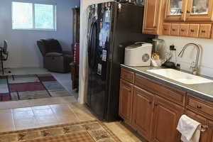 Kitchen featuring brown cabinetry, black refrigerator with ice dispenser, light tile patterned flooring, and dark stone countertops