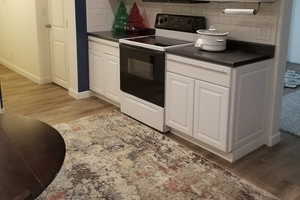 Kitchen with electric range oven, light wood-style flooring, dark countertops, and white cabinetry