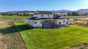 Back of property featuring a mountain view, a balcony, and a lawn