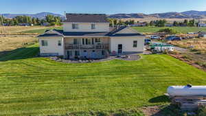 Rear view of property with a mountain view, a lawn, a balcony, and a view of rural / pastoral area