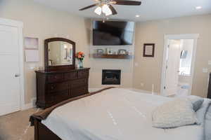 Carpeted master bedroom featuring a fireplace, ceiling fan, recessed lighting, and ensuite bathroom