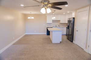 Basement apartment kitchen/dining/living area with light countertops, recessed lighting, fridge with ice dispenser, white cabinetry, and decorative light fixtures