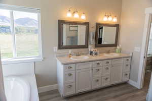 Master bathroom featuring double vanity, dark wood LVP floors, and a bath