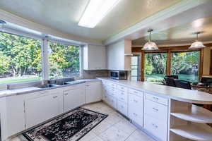 Kitchen with open shelves, light countertops, a peninsula, white cabinetry, and pendant lighting