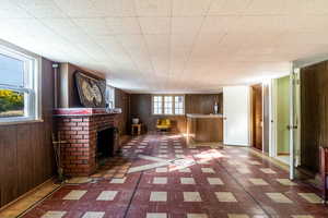 Unfurnished living room featuring wood walls, a brick fireplace, and tile patterned floors