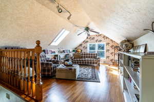 Living room featuring a skylight, wood finished floors, a textured ceiling, lofted ceiling, and track lighting