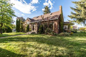 View of front of property with a front yard, a chimney, brick siding, and a shingled roof