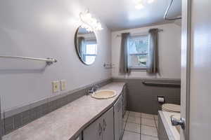 Full bath with light tile patterned flooring, tile walls, vanity, and a wainscoted wall