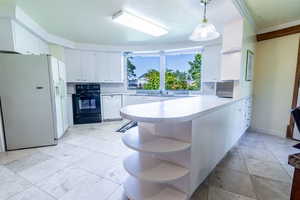 Kitchen with a peninsula, white appliances, pendant lighting, white cabinets, and light countertops