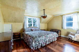 Bedroom with a textured ceiling, a textured wall, dark wood-style floors, and vaulted ceiling