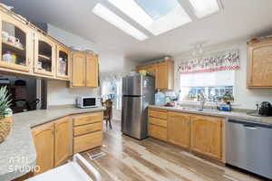 Kitchen with stainless steel appliances, light countertops, glass insert cabinets, light wood finished floors, and a skylight