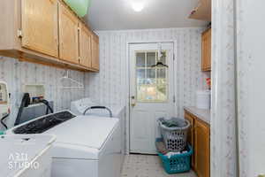 Laundry area with cabinet space, washing machine and clothes dryer, and wallpapered walls