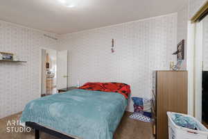 Carpeted bedroom with ornamental molding and wallpapered walls