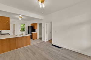 Kitchen with brown cabinetry, light countertops, light wood-style floors, black appliances, and a peninsula