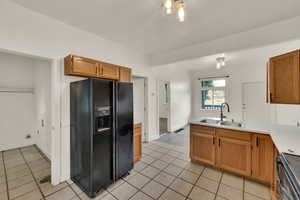 Kitchen with black fridge with ice dispenser, stainless steel range with electric cooktop, light tile patterned flooring, light countertops, and a peninsula
