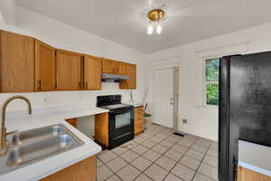 Kitchen with black appliances, light tile patterned floors, light countertops, under cabinet range hood, and brown cabinetry