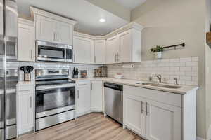 Kitchen featuring stainless steel appliances, white cabinetry, tasteful backsplash, light stone countertops, and recessed lighting