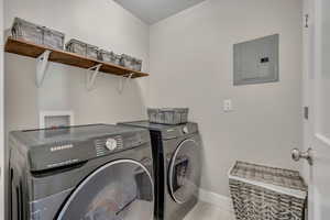 Laundry area with electric panel, washer and dryer, and light tile patterned floors