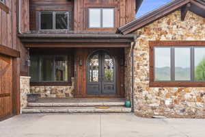 Property entrance with stone and cedar siding and a porch