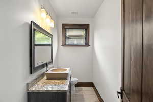 Main level Guest Bathroom with Stone sink, vanity and light tile patterned flooring