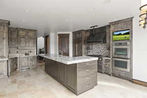 Kitchen with decorative backsplash, under cabinet range hood, stainless steel appliances, light stone counters, and recessed lighting