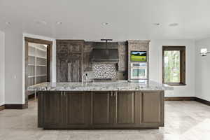 Kitchen with light stone counters, Double Ovens, ventilation hood, backsplash, and recessed lighting