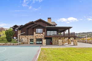 Back of house with stone and cedar siding, a yard, a chimney, and a balcony