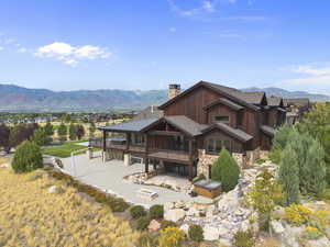Back of house with stone and cedar siding, a mountain view, a chimney, a hot tub, and a patio area