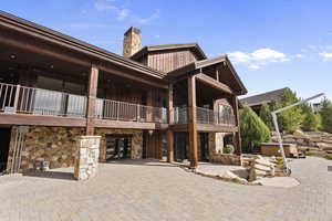 Back of property with stone and cedar siding, a balcony, a chimney, a patio area, and a hot tub
